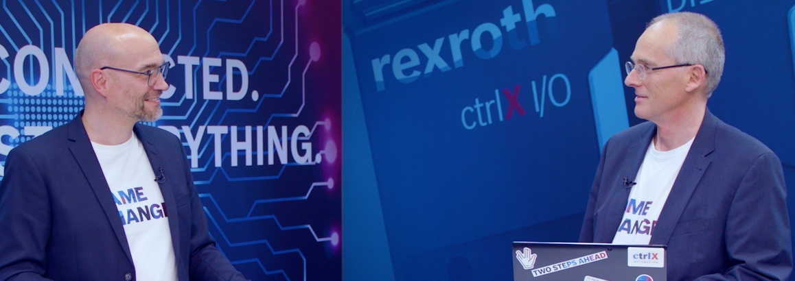Gastgeber Christian Zentraf und sein Gast Thomas Fey stehen an Besprechungstischen und sprechen über webbasierte HMI-Anwendungen zum Bedienen und Visualisieren, der Automatisierungslösung ctrlX AUTOMATION