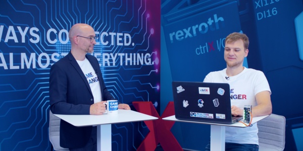 Gastgeber Christian Zentraf und sein Gast Michael Schäfer stehen an Besprechungstischen und sprechen über das Programmieren von Python-Skripten direkt auf der ctrlX CORE, der Steuerungshardware der Automatisierungslösung ctrlX AUTOMATION