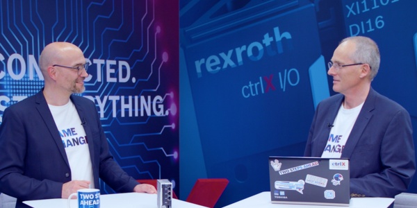 Gastgeber Christian Zentraf und sein Gast Thomas Fey stehen an Besprechungstischen und sprechen über webbasierte HMI-Anwendungen zum Bedienen und Visualisieren, der Automatisierungslösung ctrlX AUTOMATION