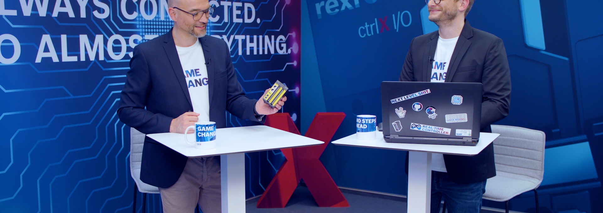 Gastgeber Christian Zentraf und sein Gast Christoph Büttner stehen an Besprechungstischen und sprechen über ctrlX SAFETY, die Sicherheitskleinsteuerung der Automatisierungslösung ctrlX AUTOMATION