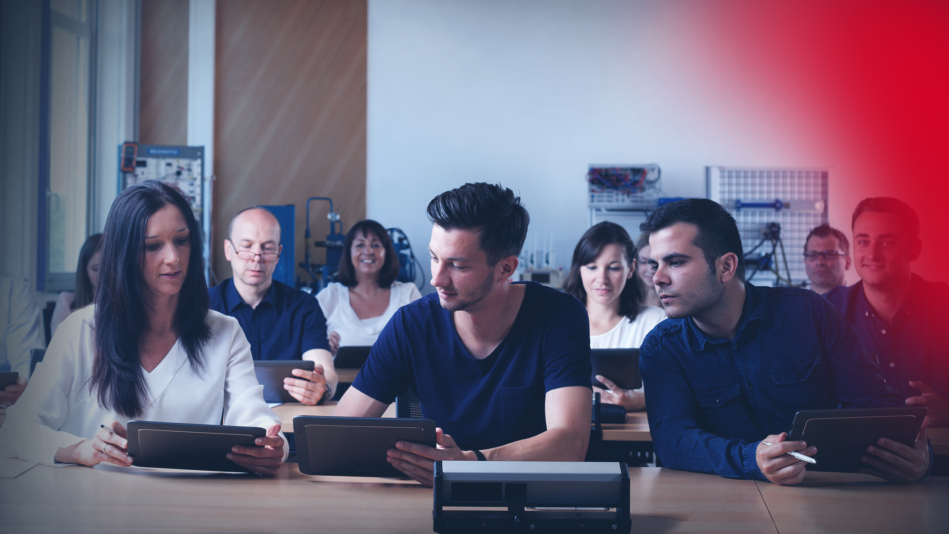Participants in a face-to-face training session sit in a training room. They use tablets to impart knowledge.