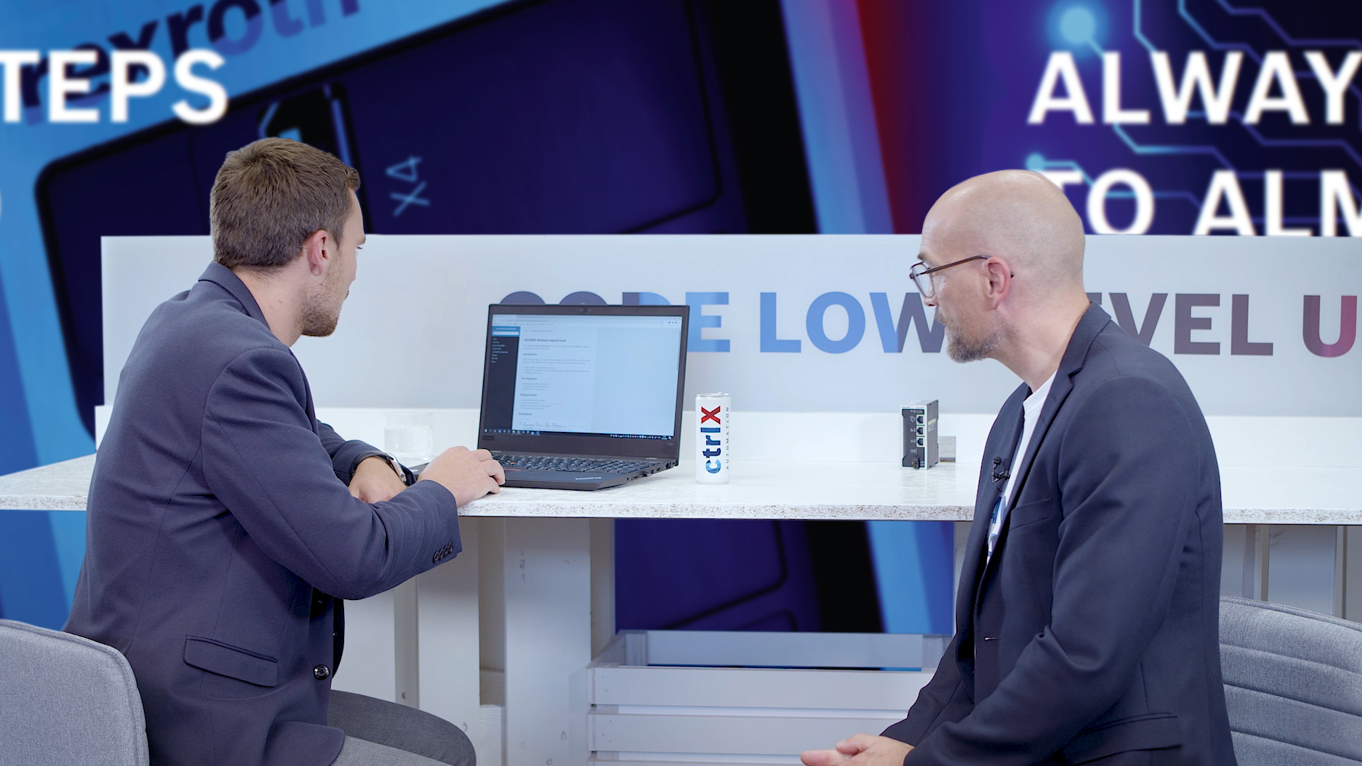 Gospodarz Christian Zentraf i jego gość Johannes Albrecht siedzą przy stole i rozmawiają o Software Development Kit (SDK) do tworzenia aplikacji dla rozwiązania automatyzacji ctrlX AUTOMATION.