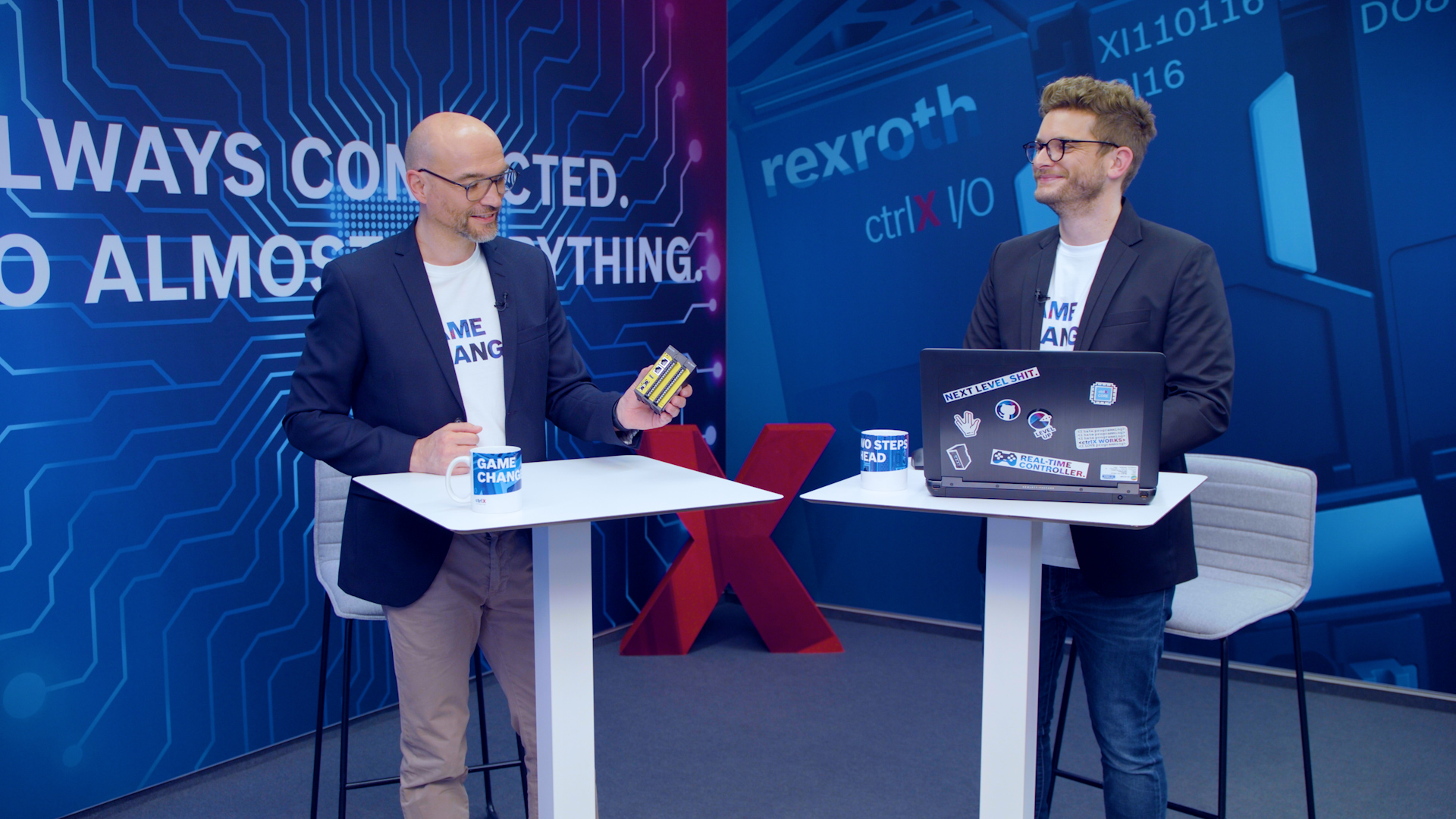 Gastgeber Christian Zentraf und sein Gast Christoph Büttner stehen an Besprechungstischen und sprechen über ctrlX SAFETY, die Sicherheitskleinsteuerung der Automatisierungslösung ctrlX AUTOMATION